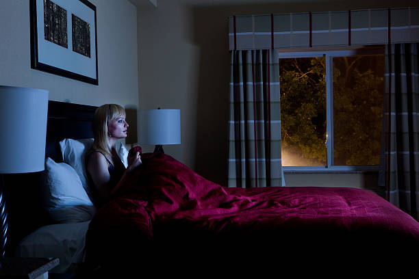 Scared Young Woman Watching TV In Her Bedroom At Night.